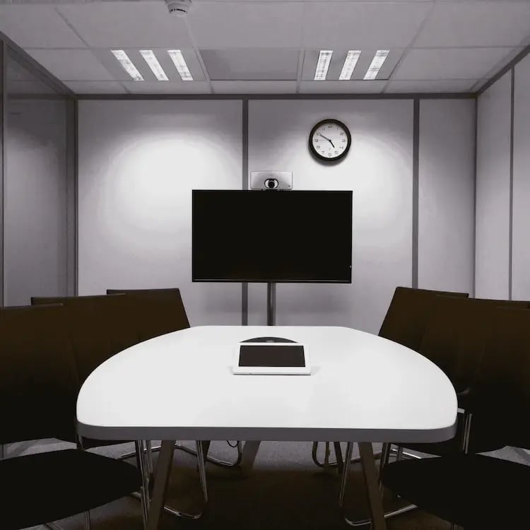 Modern school meeting room with a wall-mounted screen, conference table, chairs, and central control tablet, ready for AV-enabled collaboration.
