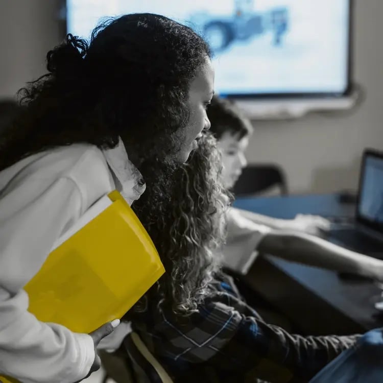 Students collaborating in a school breakout space with laptops and an interactive display screen, highlighting AV technology that supports group learning.