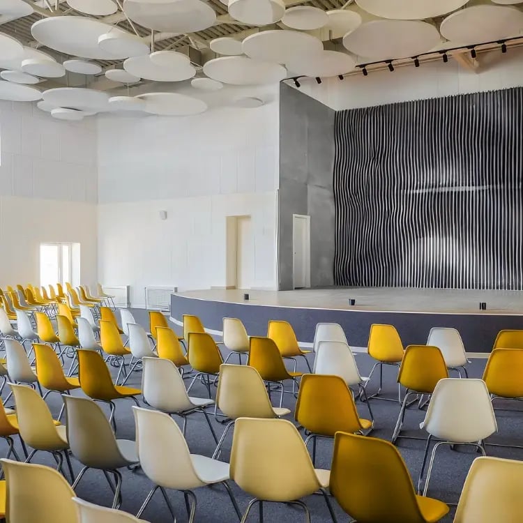 Modern school hall with stage and rows of yellow and white chairs, designed for assemblies, performances, and AV-supported events.